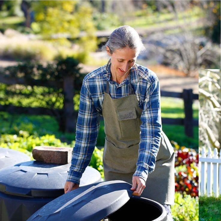 Woman in blue flannelette shirt wearing original green gardening apron whilst removing lid from a composter.This is a very hardwearing gardener apron that will be in use for many years to come. 